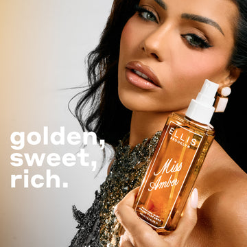 A woman with dark hair and a beaded top holds a 90mL bottle of Miss Amber perfume mist against a warm beige background, with the text 