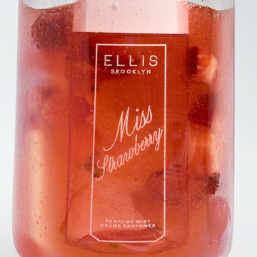 MISS STRAWBERRY Perfume Mist 90ml in a clear glass filled with red juice and cut up strawberries on a white background