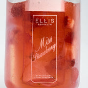 Brume parfumée MISS STRAWBERRY 90 ml dans un verre transparent rempli de jus rouge et de fraises coupées sur fond blanc