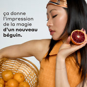 Femme aux cheveux noirs portant un bandeau et un débardeur orange et bleu tient un panier beige rempli d'oranges et d'une orange sanguine tranchée sur fond blanc avec du texte noir qui dit « ca donne I'impression de la magie d'un nouveau beguin. »