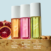 NEW CRUSH Brume Parfumée 90ml, LOVE POM Brume Parfumée 90ml, et FOREVER PISTACHIO Brume Parfumée 90ml sur un marbre beige entre des tranches de grenade, d’orange sanguine et de pistaches sur un fond bleu clair avec un texte blanc qui dit « la magie d’un nouveau beguin. Une promenade dans le chemin des amoureux. ca sent délicieusement bon pour toujours. »
