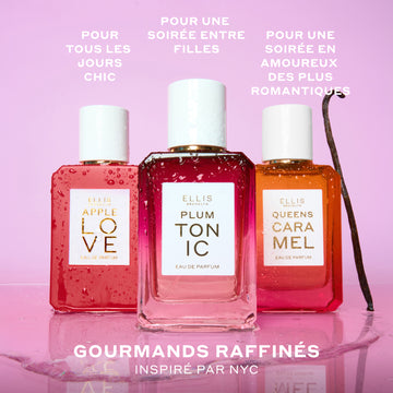 APPLE LOVE Eau de Parfum 50 ml, PLUM TONIC Eau de Parfum 50 ml et QUEENS CARAMEL Eau de Parfum 50 ml couverts de gouttes d'eau à côté d'une gousse de vanille et posés sur une flaque d'eau sur fond rose avec un texte blanc qui dit « Pour tous les jours chic. Pour une soirée entre filles. Pour une soiree en amoureux des plus romantiques. Gourmands raffinés inspirés par NYC »