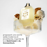 Vanilla Salt 50ml Eau De Parfum sans bouchon dans un verre avec glace à la vanille, morceaux de cône de glace, et bague en or, sur fond blanc, au-dessus d’un texte noir qui dit « Proposant une vanille salee moderne et envoutante, inspirée de la Gold Coast du Connecticut. »
