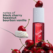 VANILLA SIN Perfume Mist 240ml with a cherry sitting on the cap, sitting on a pile of cherries and a spoon with a cherry on a pile of whipped cream with black text that reads "notes of black cherry, hazelnut, bourbon vanilla" on a pink background