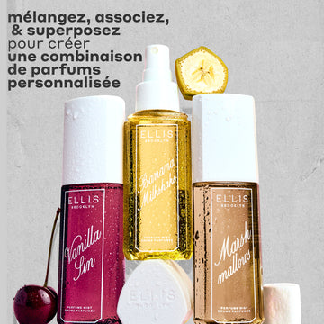Brume Parfumée VANILLA SIN 240ml à côté d'une cerise, Brume Parfumée BANANA Milkshake 240ml posée sur son bouchon, Brume Parfumée MARSHMALLOWS 240ml avec une tranche de banane dessus et une guimauve à côté, le tout couvert de gouttes d'eau sur un fond gris et rugueux avec un texte noir qui dit « melangez, associez & superposez pour creer une combinaison de parfums personnalisée. »