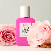 Flacon de parfum Florist 50 ml sur une table blanche avec des roses roses sur un fond blanc cassé.