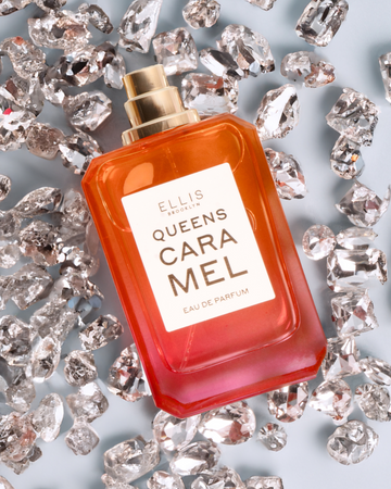 Queens Caramel Eau de Parfum 50ml without cap lays on diamonds on a blue background.