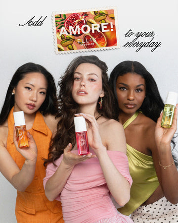 Woman with black hair wearing an orange dress and white pearl earrings holds NEW CRUSH Perfume Mist 90ml, woman with brown hair wearing a pink off the shoulder top holds LOVE POM Perfume Mist 90ml, and woman with brown hair wearing green tank top and white and black skirt holds FOREVER PISTACHIO Perfume Mist 90ml on a white background with a stamp with drawn pistachios, blood oranges, and pomegranates with white text that reads "Amore! and Ellis Brooklyn" between black text that reads "Add to your everyday"