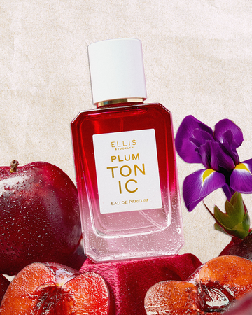 PLUM TONIC Eau de Parfum 50ml on top of red velvet between sliced plums, a whole plum, and a purple iris flower on a textured beige background