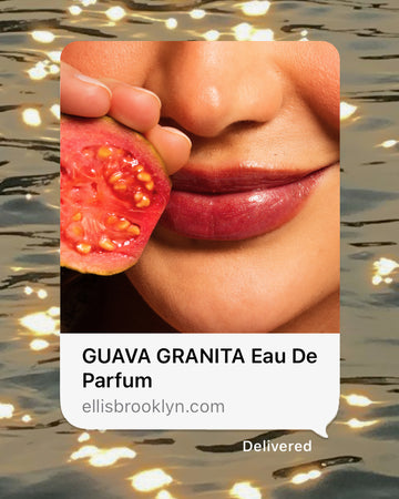 Closeup photo of a person holding a sliced guava near their lips, with black text that reads 'GUAVA GRANITA Eau De Parfum' and 'ellisbrooklyn.com' on a white text bubble over a water background with warm lights.