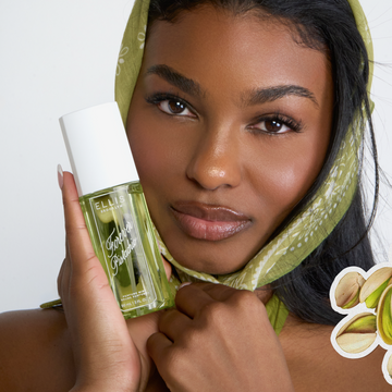 Woman with black hair wearing a green scarf on her head and holding a bottle of FOREVER PISTACHIO Perfume Mist 90ml against her cheek overlaid with a drawn image of pistachios on a white background