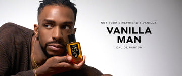 Model with brown hair weaing gold necklaces, bracelets, rings, and brown sweater holding Vanilla Man 50ml Eau De Parfum in one hand next to face, on white background with black text that reads "Not Your Girlfriend's Vanilla. Vanilla Man Eau De Parfum"