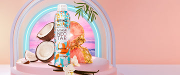 Amika x Ellis Brooklyn Miami Nectar Perk Up Dry Shampoo on pink pedestal with vanilla beans, coconut, pine pineapple, and flowers on white table against neon arch and pink sunset and palm leaves, on pink background.