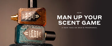Vanilla Man 50ml Eau De Parfum with cap removed on top of Worth Avenue 50ml Eau De Pafum on top of dumbbell covered with wate droplettes, on brown background with white text that reads "New! Man Up Your Scent Game A New Take on Men's Fragrance."