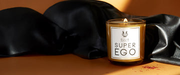 Super Ego Terrific Scented candle in front of back satin, on orange background.