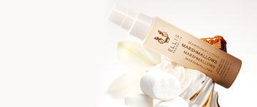 Marshmallows Perfume Mist 50ml on pile of whipped cream, 3 marshmallows, flower, and caramel on a white background