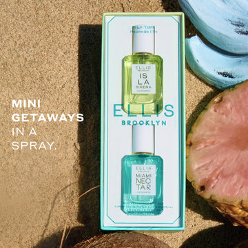 ISLA TIME by Ellis Brooklyn gift set featuring a light blue-green box containing a mini-7.5mL bottle of ISLA SIRENA eau de parfum and a mini-7.5mL bottle of MIAMI NECTAR eau de parfum. The set is styled on a sandy beach background with a sliced pink pineapple, a blue banana, and a coconut.
