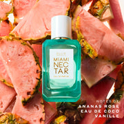 Flacon de 50 mL d'Eau de Parfum MIAMI NECTAR, entouré de tranches d'ananas rose sur un fond blanc avec un texte indiquant « Notes de ananas rose, eau de coco, vanille »