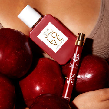 Modèle portant un débardeur marron tenant des pommes, Apple Love 50ml Eau de Parfum, et Apple Love 10ml Eau de Parfum en spray voyage contre sa poitrine.