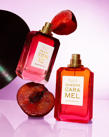 PLUM TONIC Eau de Parfum 50ml without cap on top of sliced plum next to QUEENS CARAMEL Eau de Parfum 50ml without cap on purple background with sliced plum and black vinyl disc in the air.