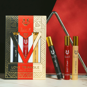 Boîte trio de parfums en roll-on Love Triangle en noir, rouge, beige et or, montrant le roll-on Myth 10 ml, le roll-on Apple Love 10 ml et le roll-on Vanilla Milk 10 ml, avec un triangle en métal sur une table en marbre noir et blanc, sur un fond noir et rouge.