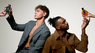 Model with brown hair wearing brown suede jacket, gold rings and gold neckalce being handed Vanilla Man 50ml Eau De Parfum leaning on model with brown hair weaing silver earrings and grey jacket being handed Worth Avenue 50ml Eau De Parfum.