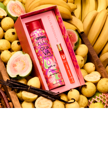 Amika x Ellis Brooklyn GUAVA GRANITA Perk Up Dry Shampoo and GUAVA GRANITA Eau de Parfum 10ml gift set lays in brown wooden bin filled with bananas, whole and sliced guavas, a bundle of vanilla beans, and almonds in a brown basket