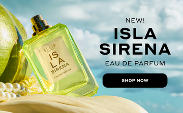 ISLA SIRENA Eau de Parfum 50ml without cap leans against a green coconut and white pearls on top of tan fabric against a blue sky and white cloud background with black text that reads 'New! ISLA SIRENA Eau de Parfum' and a black oval with white text that reads 'Shop Now'