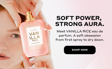 Woman with red hair and pale pink manicure holds VANILLA RICE Eau de Parfum 50ml without cap above her head with black text that reads "Soft power, strong aura. Meet VANILLA RICE eau de parfum. A soft obsession from first spray to dry down." and a black circle with white text that reads 'Shop Now" all on a pink background