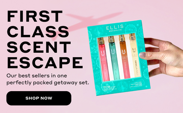 Hand holding FIRST CLASS Gift Set containing GUAVA GRANITA Eau de Parfum 10ml, MIAMI NECTAR Eau de Parfum 10ml, QUEENS CARAMEL Eau de Parfum 10ml, and VANILLA SALT Eau de Parfum 10ml with black text that reads 'FIRST CLASS SCENT ESCAPE. Our best sellers in one perfectly packed getaway set' and a black oval with white text that reads 'Shop Now' all on a pink background with a shadow of an airplane