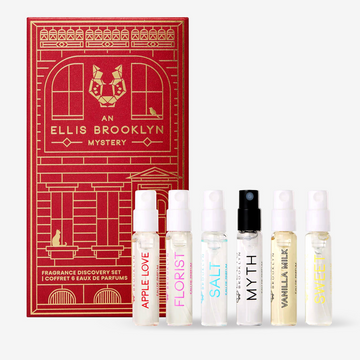 Flacon d'Eau de Parfum Apple Love 1,5 ml, flacon d'Eau de Parfum Florist 1,5 ml, flacon d'Eau de Parfum Salt 1,5 ml, flacon d'Eau de Parfum Myth 1,5 ml, flacon d'Eau de Parfum Vanilla Milk 1,5 ml et flacon d'Eau de Parfum Sweet 1,5 ml devant une boîte rouge du coffret de découverte de parfum mystère An Ellis Brooklyn.