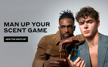 Model with brown hair wearing brown suede jacket and gold rings holding Vanilla Man 50ml Eau De Parfum in one hand leaning on shoulder of model with brown hair weaing silver earrings and grey jacket holding Worth Avenue 50ml Eau De Parfum on light grey background next to black text that reads "Man Up Your Scent Game" and black rectangle with white text that reads "Join The Waitlist"