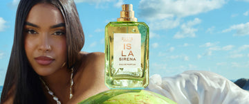 Woman with brown hair wearing a white shell halter neck bikini top and white skirt lays down on her side with ISLA SIRENA Eau de Parfum 50ml without it's cap and the sun shining through it on a green coconut in front of her with a blue sky and white clouds in the background