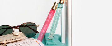 GUAVA GRANITA Eau de Parfum 10ml and MIAMI NECTAR Eau de Parfum 10ml lean against suitcase handle next to airplane boarding pass, gold wallet, and tortoiseshell sunglasses on top of teal suitcase on a white background