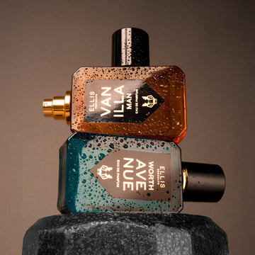 Vanilla Man 50ml Eau De Parfum with cap removed on top of Worth Avenue 50ml Eau De Pafum on top of dumbbell covered with wate droplettes, on brown background.