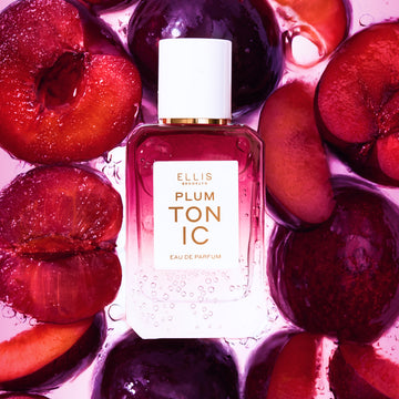 PLUM TONIC Eau de Parfum 50ml surrounded by sliced plums all under water with bubbles on a pink background