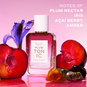 PLUM TONIC Eau de Parfum 50ml next to sliced plums, amber stones and a purple iris covered in water droplets on a pink background with white text that reads "Notes of plum nectar, iris, açaí berry, amber"