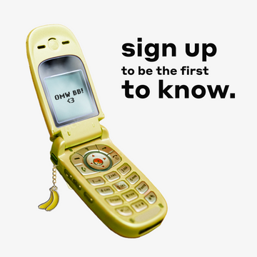 Yellow flip phone with banana charm open to a text that reads "OMW BB! <3" on a white background with text that reads "sign up to be the first to know."