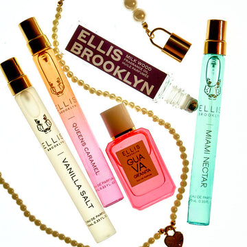 Pearl charm necklace surrounded by Vanilla Salt 10ml Travel Spray, Queens Caramel 10ml Travel Spray, Guava Granita 7.5ml Eau De Parfum Mini Dabber, Milk Wood Fragrance Oil Rollerball without cap, and Miami Nectar 10ml Eau De Parfum Travel Spray, on white background.