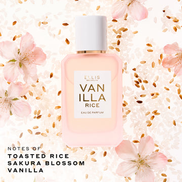 Ellis Brooklyn Vanilla Rice Eau de Parfum 50mL bottle in a soft blush pink glass with a white cap, centered on a background of white ad brown rice grains and pink blossoms. Text at the bottom left corner reads 'NOTES OF TOASTED RICE SAKURA BLOSSOM VANILLA'.