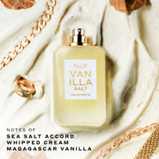 Vanilla Salt Eau de Parfum 50mL bottle displayed on a cream-colored frosting background with gold jewelry and waffle pieces, with black text in the bottom left corner that reads “notes of sea salt accord, whipped cream, Madagascar vanilla.”