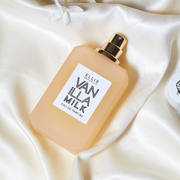 Lait à la vanille 50 ml Eau de Parfum avec le bouchon retiré sur un drap en satin blanc près d'une fleur blanche.