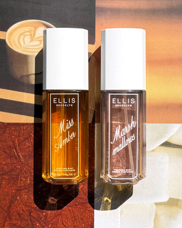 MISS AMBER perfume mist 90mL bottle next to a 90mL bottle of COCOA BLANCO perfume mist set against a split warm-toned background with coffee, red saffron, and a orange sunset collage. 