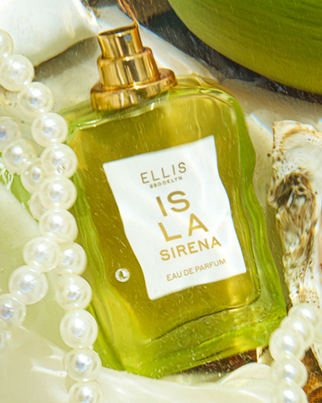 ISLA SIRENA Eau de Parfum 50ml without cap sits on white fabric next to white pearls, a white shell, and a green coconut all under water