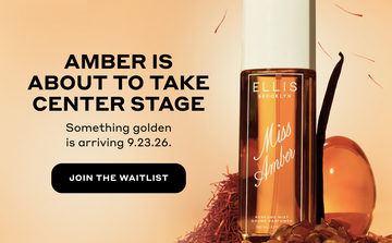 240mL Miss Amber Perfume Mist bottle standing with a vanilla bean, red saffron, and amber colored stones on yellow background with black text that reads "Amber is about to take center stage. Something golden is arriving 9.23.26." and a black oval with white text that reads "Join The Waitlist"