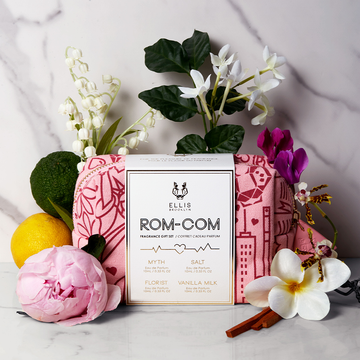 Sac du coffret parfum Rom-Com à motifs rouges et roses sur fond de marbre blanc et gris avec des fleurs blanches, roses, violettes et jaunes, bois de santal, citron et bergamote.