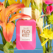 IMAGE 4: FLORIST 50ML BOTTLE WITH FLOWERS AND BLUE BACKDROP