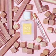 Iso Gamma Super 50ml Eau De Parfum and Iso Gamma Super 10ml Eau De Parfum Travel Spray next to square and rectangular wooden blocks, on pink background.