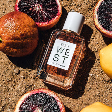West 50ml Eau De Parfum on dirt next to blood oranges and lemon.